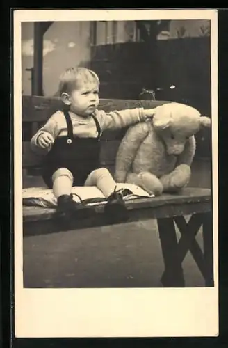 AK Kleiner Junge in kurzer Latzhose mit gleichgrossem Teddybär auf einer Bank