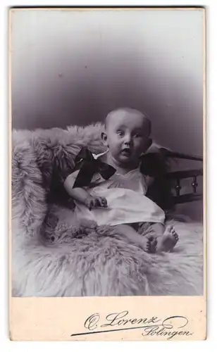 Fotografie Otto Lorenz, Solingen, Kaiserstr. 259, überrascht guckendes Baby auf Felldecke sitzend