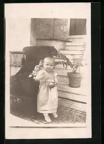 Foto-AK Kleinkind mit Puppe neben Sessel