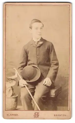 Fotografie H. Spink, Brighton, Western Road 109, Junger Mann im Anzug mit Spazierstock und Melone in der Hand