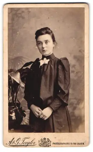 Fotografie A & G. Taylor, Brighton, Kings Road 34, Junge Frau mit ernstem Blick im dunklen Kleid mit Puffärmeln