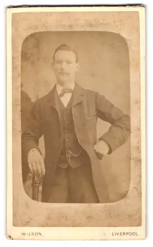 Fotografie M. W. Wilson, Liverpool, Upper Duke Street 1, Junger Mann im Dreiteiler mit in die Seite gestützter Hand