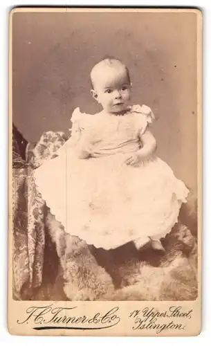 Fotografie Turner & Co, Islington, 17. Upper Street, Kleinkind im weissen Kleid auf Pelzdecke
