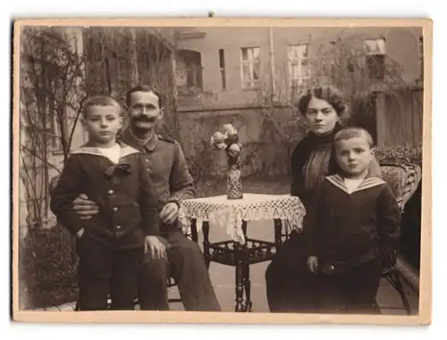 Fotografie unbekannter Fotograf und Ort, Soldat in Uniform posiert mit seinen beiden Kindern und Frau im Hof
