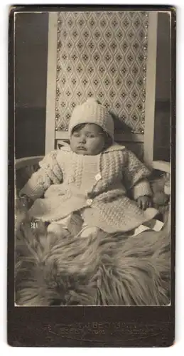 Fotografie Beckmann, Essen, Frohnhauserstrasse 7 u. 11, Baby mit Mützchen im Strickkleid auf einem Fell