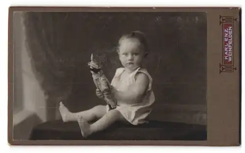Fotografie Karl Enz, Weinfelden, Kleinkind in weissem Trägerkleidchen mit Puppe