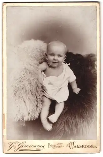 Fotografie G. Gronemann, Walsrode, Süsses Kleinkind im Hemd sitzt auf Fell