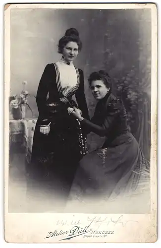 Fotografie Atelier Düll, München, Blüthenstr. 21, zwei junge Frauen in dunklen Kleidern in einer Studiokulisse, 1901