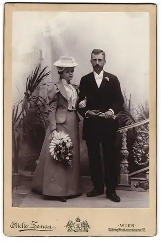 Fotografie Atelier Zeman, Wien, junges Paar im Anzug mit Fliege und im Kleid mit Hut, Blumenstrauss