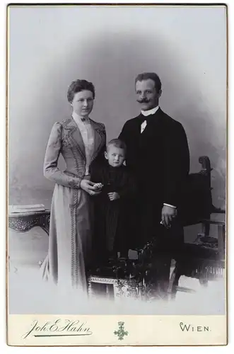 Fotografie Joh. E. Hahn, Wien, junge Eltern mit ihrem Kind im karierten Kleid posieren im Atelier