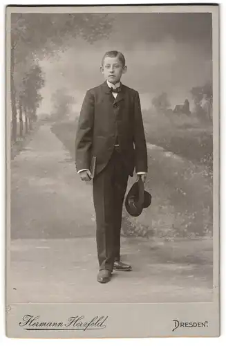 Fotografie Hermann Herzfeld, Dresden, Junge im Anzug mit Fliege und Hut vor einer Studiokulisse