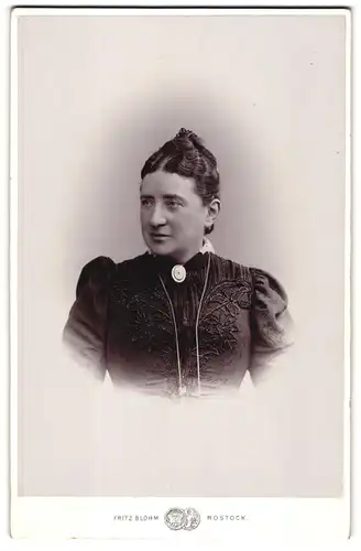 Fotografie Fritz Blohm, Rostock, Dame im bestickten Kleid mit Brosche und Hochgesteckten Haaren