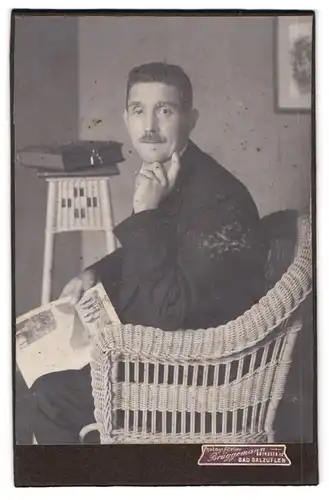 Fotografie Brüggemann, Bad Salzuflen, Herr im Anzug posiert im Rattansessel mit Fotoalbum in der Hand