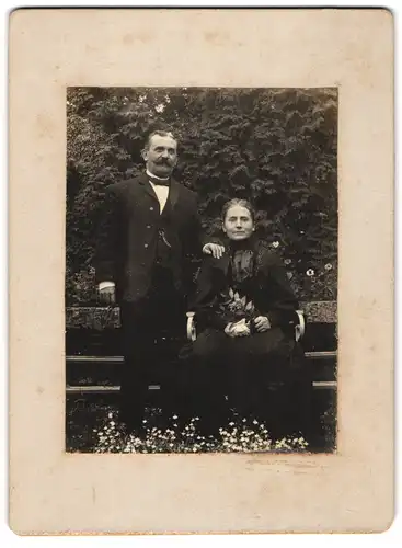Fotografie unbekannter Fotograf und Ort, älteres Ehepaar im schwarzen Kleid und Anzug posiert im Garten