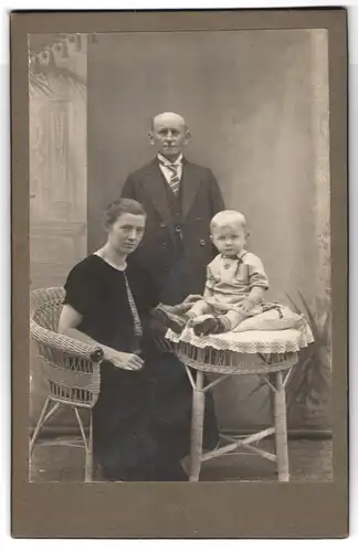 Fotografie unbekannter Fotograf und Ort, Familien-Portrait, Elternpaar und kleiner blonder Knabe auf Tisch sitzend