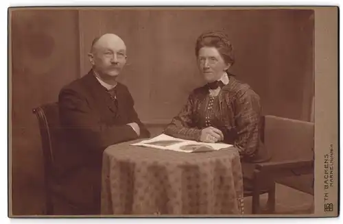 Fotografie Th. H. Backens, Marne i. Holstein, Älteres Paar in hübscher Kleidung am Tisch