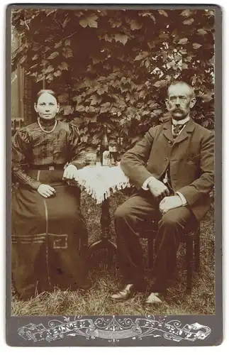 Fotografie unbekannter Fotograf und Ort, Älteres Paar in modischer Kleidung am Gartentisch
