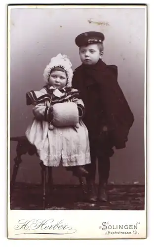 Fotografie H. Herber, Solingen, zwei niedliche Kinder in Winterkleidung mit Muff und Mantel