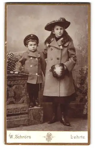 Fotografie W. Schrörs, Lehrte, junge Geschwister in Winterkleidung mit Muff und Peitsche