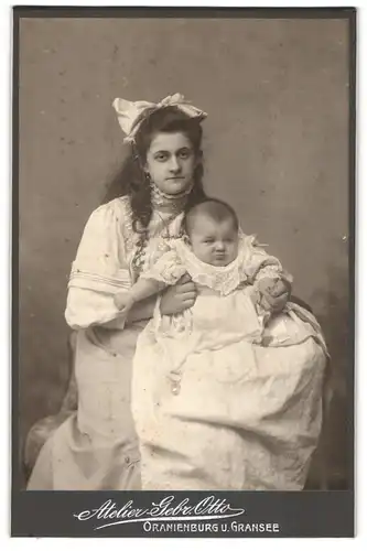 Fotografie Geb. Otto, Oranienburg, junge Mutter im weissen Kleid mit Haarschleife und Kind auf dem Schoss, Mutterglück