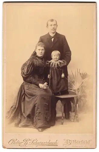 Fotografie R. Schwarzbach, Bitterfeld, Kaiserstr. 14, junge Eltern in feiner Kleidung mit ihrer Tochter auf dem Stuhl