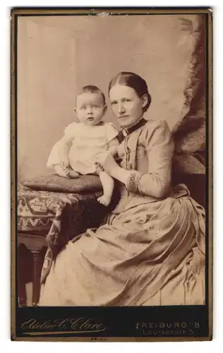 Fotografie C. Clare, Freiburg i. B., Mutter im Biedermeierkleid mit Kleinkind auf dem Tisch, Mutterglück