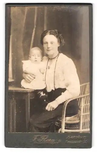 Fotografie F. Flarupe, Flensburg, Portrait junge Mutter in weisser Bluse mit Neugeborenen auf dem Tisch, Mutterglück