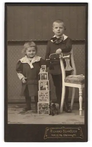 Fotografie Richard Schröder, Halle a. S., Geschwisterpaar in Kleidern mit Blechtrompete und Spielzeugwürfeln