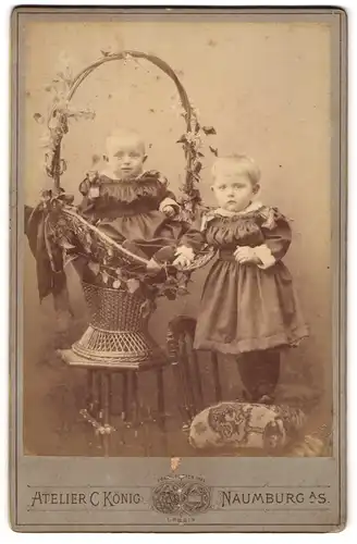 Fotografie C. König, Naumburg a. S., zwei niedliche Kinder in dunklen Kleidern, sitzend im Weidenkorb