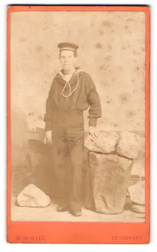 Fotografie W. H. Gill, Devonport, Portrait junger Matrose in Uniform posiert in einer Studiokulisse