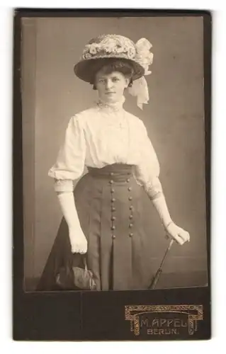 Fotografie M. Appel, Berlin, junge Frau in heller Bluse mit dunklem Rock und geschmücktem Hut samt Handtasche