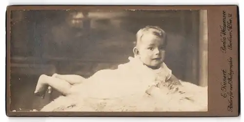 Fotografie E. Kunert, Berlin-Weissensee, Berliner Allee 31, Portrait blondes Baby im Hemdchen auf einem Fell liegend