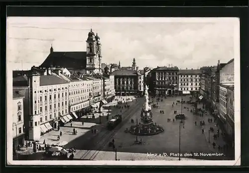 AK Linz a. d. D., Platz d. 12. November mit Geschäften und Denkmal, Strassenbahn