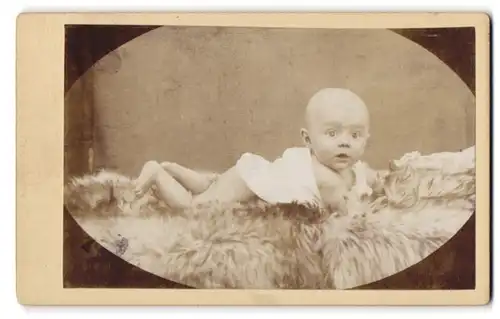 Fotografie unbekannter Fotograf und Ort, Portrait süsses Baby im Hemdchen auf einem Fell liegend