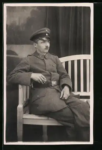 Foto-AK Rauchender Soldat des XII.13. Landwehrregiments in Feldgrau auf Bank sitzend