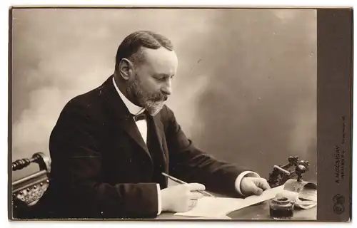 Fotografie A. Mocsigay, Hamburg, Neuwerwall 46, Älterer Herr im Anzug mit Vollbart am Schreibtisch
