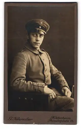 Fotografie G. Neunaber, Hildesheim, Paradeplatz 14, Junger Soldat in Feldgrau mit Schirmmütze auf einem Stuhl sitzend