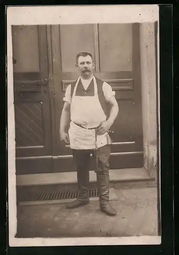 AK Fleischermeister in Schürze mit Messertasche vor einem Haus stehend