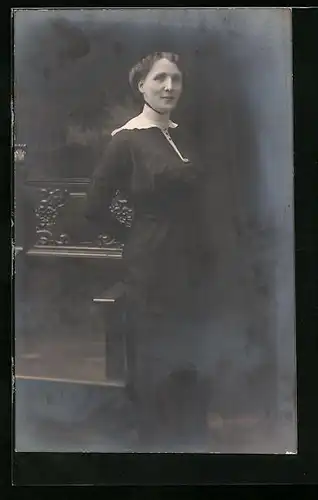 Foto-AK Schöne Frau steht an einer stilvoll verzierten Bank, Studiokulisse