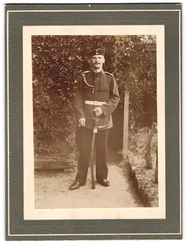 Fotografie unbekannter Fotograf und Ort, Rauchender Soldat in Uniform mit Krätzchen, Schützenschnur und Säbel