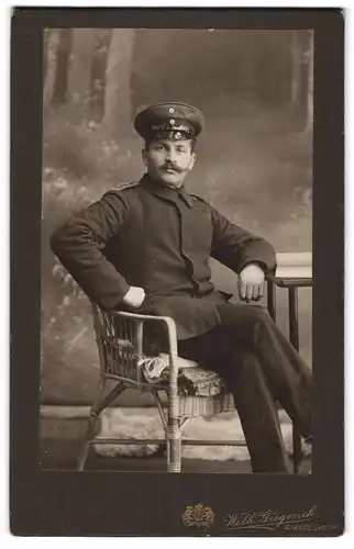 Fotografie Wilh. Giegerich, Ingelheim, Sitzender Soldat in Feldgrau mit Schirmmütze