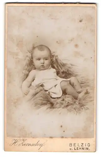 Fotografie H. Zernsdorf, Belzig, Sandbergerstr. 23, Süsses Kleinkind im Hemd liegt auf Fell