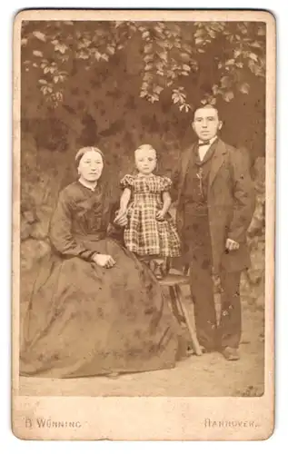 Fotografie B. Wünning, Hannover, Artilleriestr. 18, Ehepaar mit Kind vor Studiokulisse