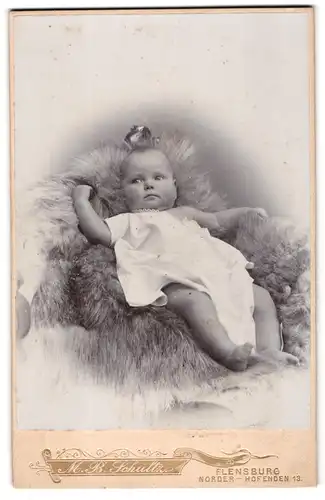 Fotografie M. B. Schultz, Flensburg, Norderhofenden 13, Süsses Kleinkind im Hemd liegt auf Fell
