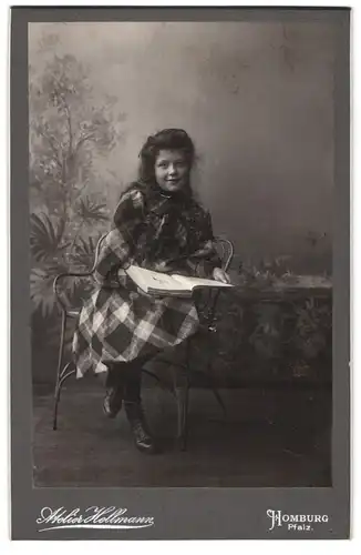 Fotografie Jacob Hellmann, Homburg /Pf., Lächelndes Mädchen in festlichem karierten Kleid mit einem Bildband