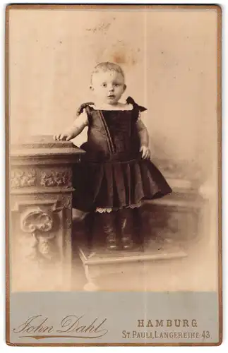 Fotografie John Dahl, Hamburg, Langereihe 43, Kleines Kind mit kurzen Haaren in weitem Kleidchen und Stiefeln