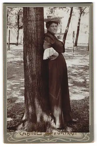 Fotografie unbekannter Fotograf und Ort, Dame mit Hut, an einen Baum gelehnt
