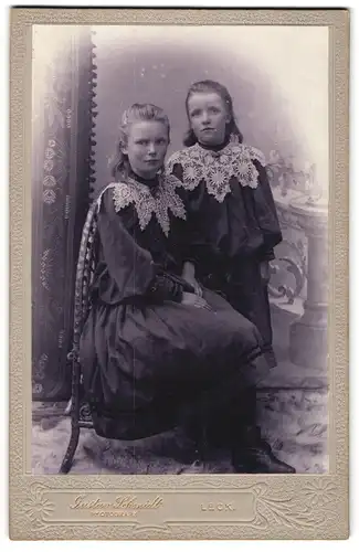 Fotografie Gustav Schmidt, Leck, Zwei Mädchen in festlichen Kleidern mit Spitzenbesatz