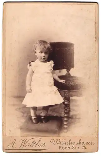 Fotografie A. Walther, Wilhelmshaven, Roon-Strasse 75, Kleinkind im weissen Kleid neben Stuhl