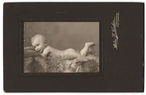 Fotografie E. Fischer, Zwenkau /S., Nacktes Baby, bäuchlings auf einem Fell liegend